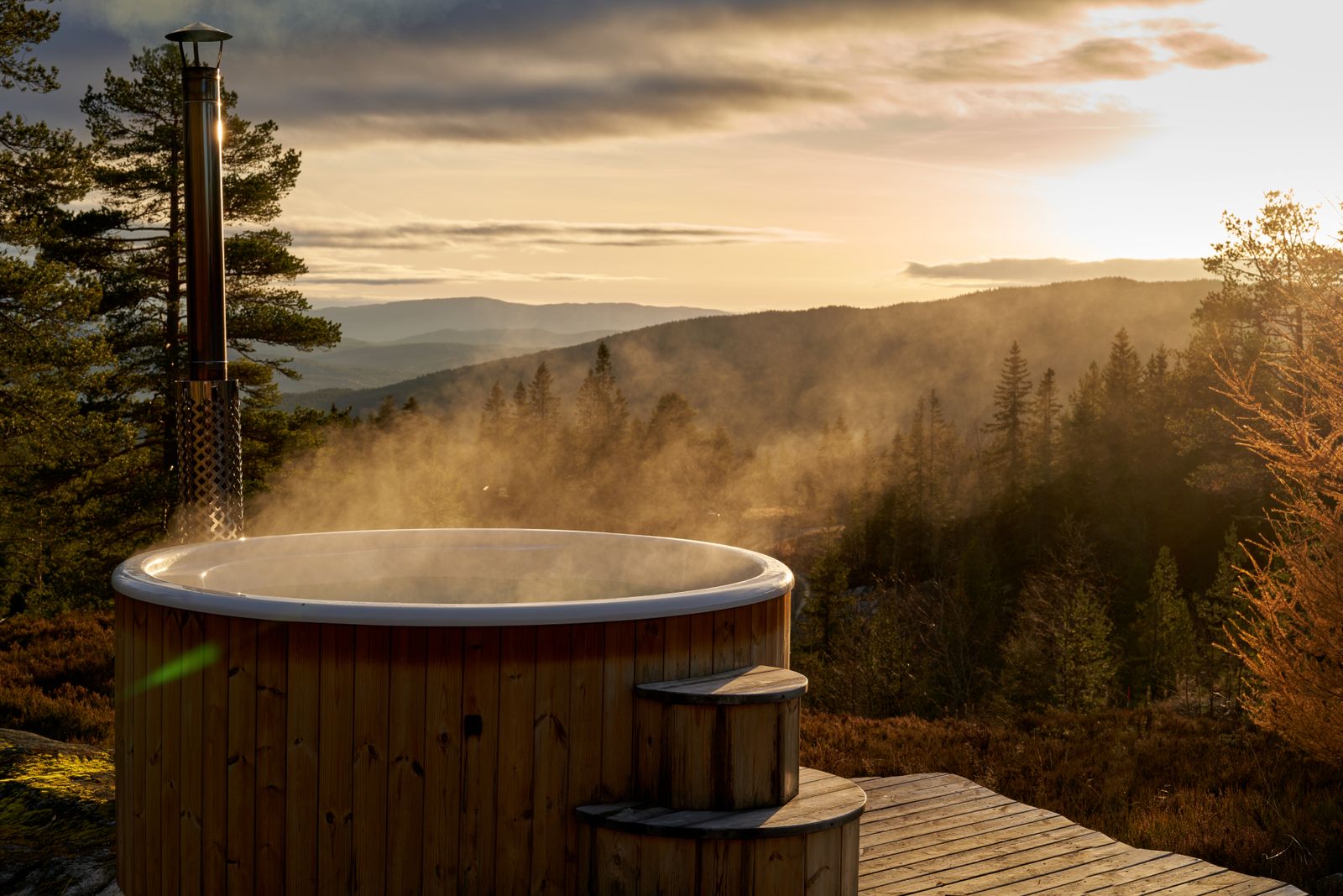 A steaming hot tub amidst the serene Norwegian countryside at sunset, offering stunning views.